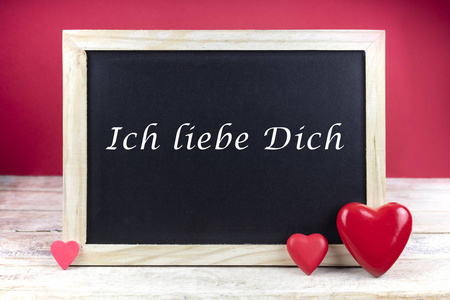木制黑板，红心，用德语写句子Ichliebedic，意思是我爱你，红色背景。