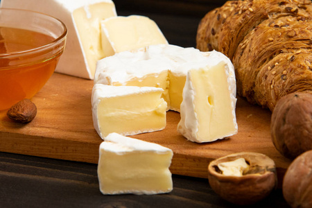 切片奶酪布里或卡蒙伯与牛角面包，蜂蜜和坚果在船上切割，在黑暗的木制背景。