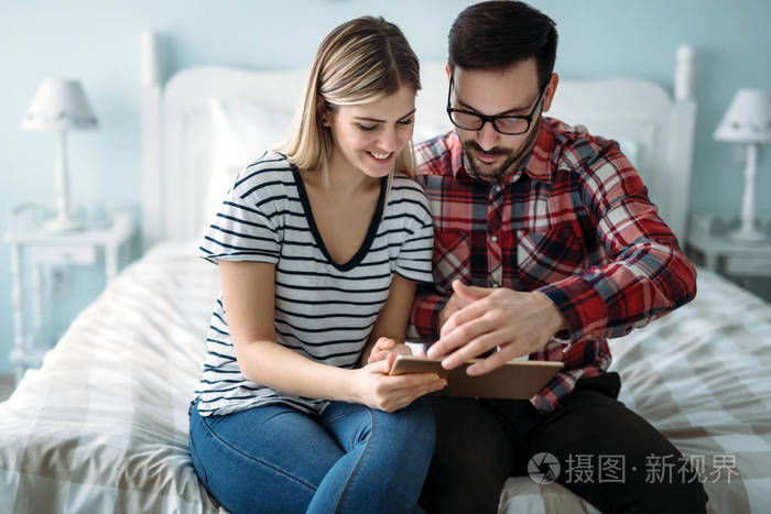 年轻的幸福夫妇在卧室里用数码平板电脑