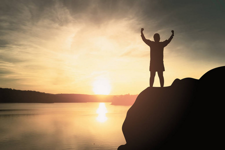 在天空日落期间,女人站在岩石上张开手的剪影成功的概念.照片