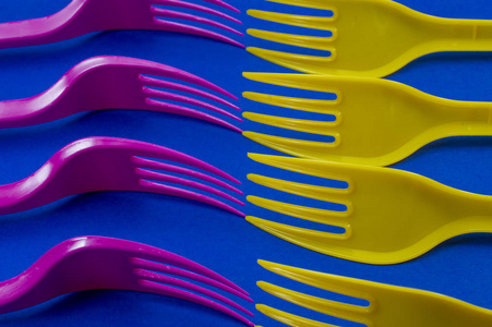 黄色和粉红色的餐具塑料叉子布置在蓝色背景上。 颜色趋势和塑料废物问题的概念