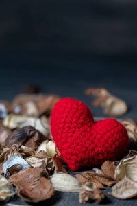 手工制作的红心由纱线制成，干燥的叶子和花放在黑色的木桌上。 爱和情人节的概念。 文本和内容的复制空间
