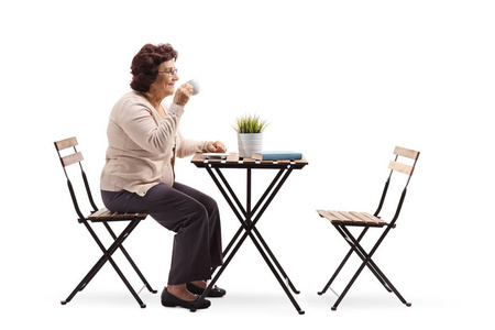 一位年长妇女在一张白色背景的桌子上喝咖啡的完整照片