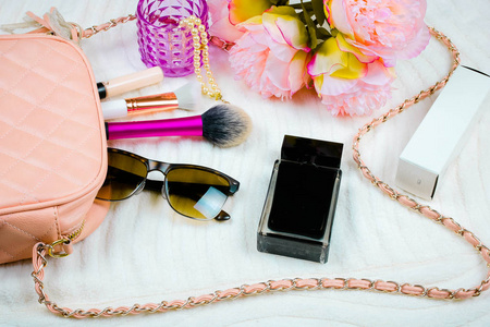 时尚概念平躺的粉红色皮革女人袋打开与太阳镜，香水刷和花在白色背景。