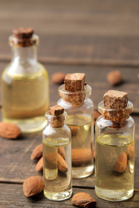 天然杏仁油在玻璃瓶和新鲜杏仁坚果靠近棕色木桌。