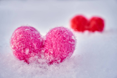 冬天，两颗红色和粉红色的羊毛心站在白色蓬松的雪上。 爱的象征。 爱海尔特卡夫情人节的概念。