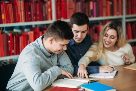 大学学生一起坐在桌旁的书和笔记本。快乐的年轻人做小组学习在图书馆