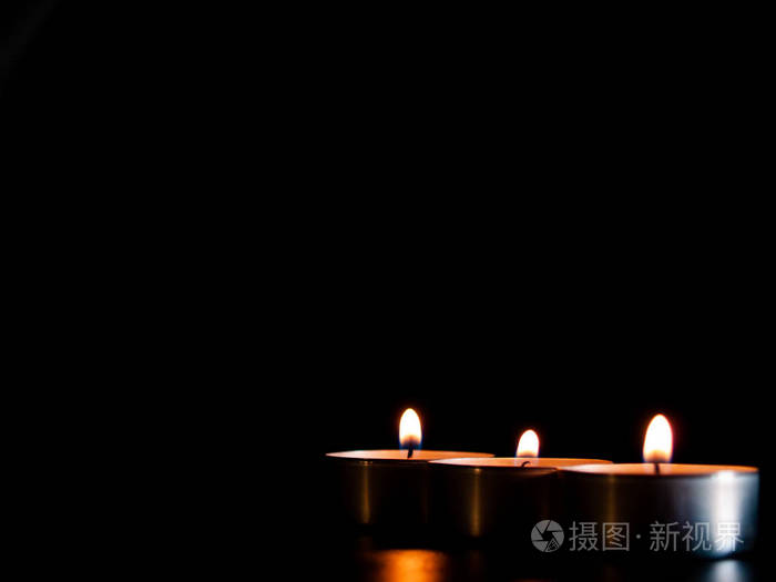 三支点燃的蜡烛,带着橙色的火焰,孤立在黑色的背景上
