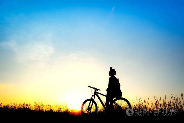 在天空日落背景下,骑自行车的女孩在田野上的剪影.