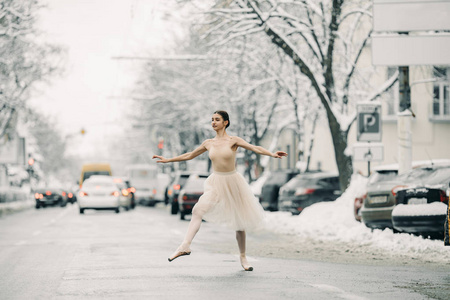 美丽的芭蕾舞女演员穿着透明的裙子，在雪城的街道上汽车里跳舞。