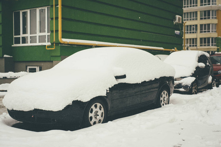 在建筑物附近的一排汽车，被雪覆盖，主要是黑色的轿车在焦点上。