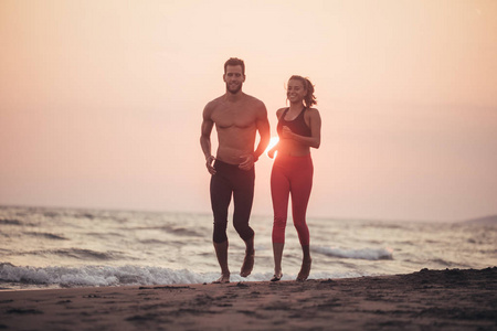 英俊的白种人男人和美丽的女人在日落时一起在沙滩上跑步。