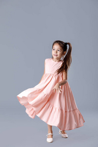 在灰色背景摆姿势的粉红色礼服的小女孩