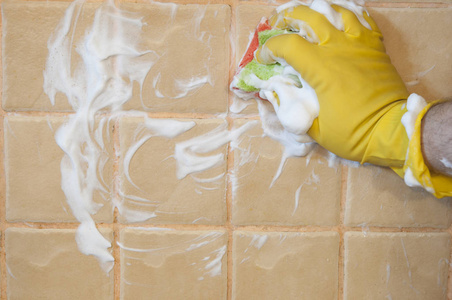戴黄色橡胶手套的人的手被用来转换瓷砖墙上的擦洗清洁。 清洁概念。
