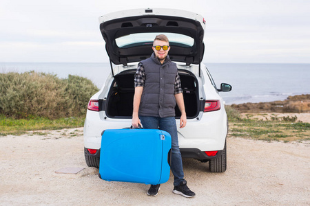 旅行假期和度假概念男子靠近带蓝色手提箱的汽车。