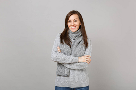 年轻女子戴着灰色毛衣围巾，双手抱着，孤立地折叠在灰色墙壁背景工作室的肖像上。 健康时尚生活方式人真诚情感冷季观念。 模拟复制空间