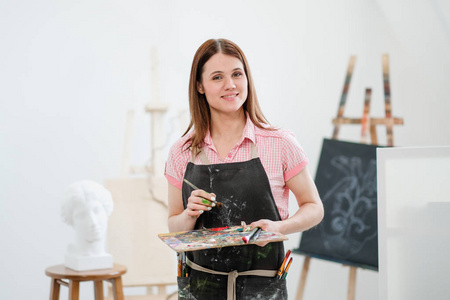 一位年轻的女画家在明亮的白色工作室里在画架上的画布上画一幅画