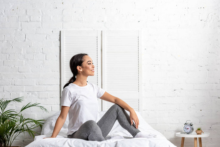 穿着白色T恤和灰色裤腿的亚洲女人，早上锻炼后坐在床上休息