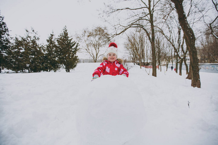 性格开朗的小女孩冬天穿着温暖的衣服和帽子，在雪地公园或户外森林里玩雪球堆雪人。 假日的冬季乐趣休闲。 家庭生活方式观念