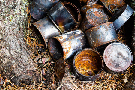 树下罐头食品用生锈的旧金属罐。 人类对森林的污染对自然的影响。
