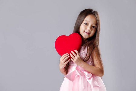 可爱的小女孩在粉红色的礼服拿着一个纸的心