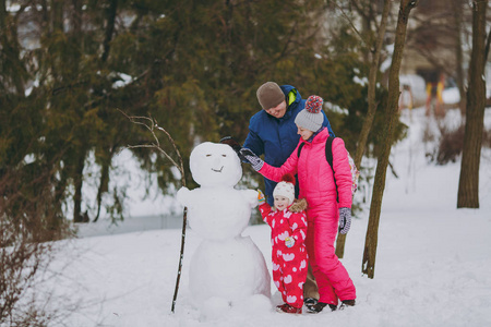 幸福的家庭男人女人小女孩穿着冬天温暖的衣服，在雪地公园或户外森林里堆雪人。 假日的冬季乐趣休闲。 家庭生活方式观念