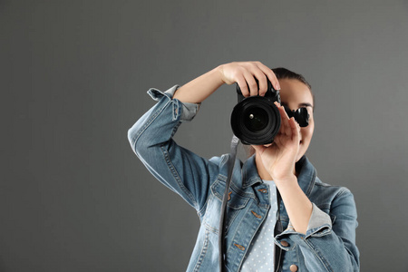 年轻的女人带着相机对着灰色的背景。 专业摄影工作室