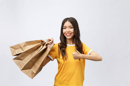 照片上, 兴奋的漂亮年轻女士站在白色背景上, 拿着购物袋。显示竖起大拇指的相机