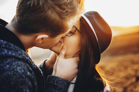 年轻人在日落时站在模糊的自然背景上激情地亲吻漂亮的女朋友。年轻夫妇在乡下接吻
