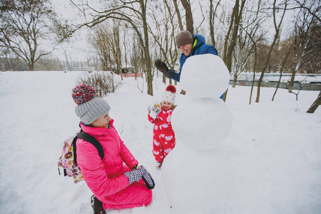 开朗的家庭男人女人，小女孩在冬天保暖衣服玩耍，在雪地公园或森林户外堆雪人。冬季好玩，节假日休闲..家庭生活方式的概念