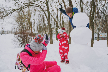 吝啬的家庭，男人，女人和穿着温暖衣服的小女孩，在公园或森林户外扔雪球堆雪人。冬季好玩，节假日休闲..家庭生活方式的概念