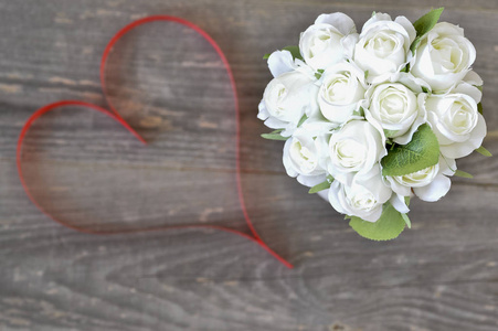 白色玫瑰花束与丝带紧密结合，在木制复古背景上以活珊瑚的心脏颜色的形式出现。 浪漫卡片概念。 从顶部的视图。 平躺着。