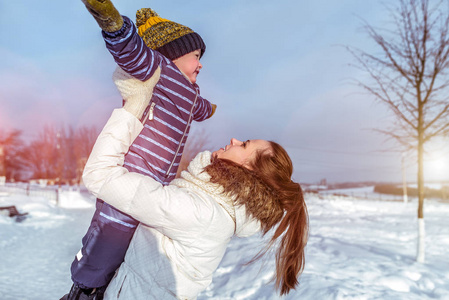 年轻的母亲笑得很开心, 抱着一个25 的男孩, 在外面的冬天玩耍。在大自然中的冬日早晨休息。他们玩飞机