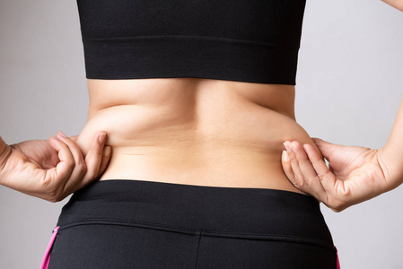 胖女人的手握着过多的腹部脂肪。 保健和妇女饮食生活方式的概念，以减少腹部和塑造健康的胃肌。