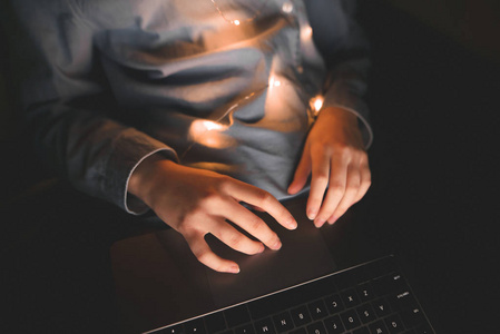 女人晚上在床上使用笔记本电脑，俯视着双手紧闭。 女人的手指在笔记本电脑的触控板上。 笔记本电脑小工具手闭上。