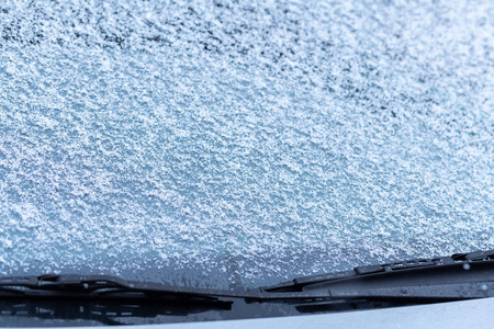 雪覆盖的车窗与雨刷宏观关闭。 防冻液没有使用。 雪地里的车辆。 冬天的时间来了。 恶劣天气条件