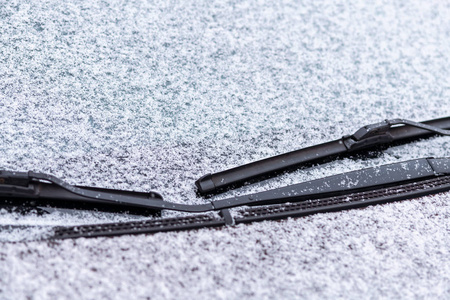 雪覆盖的车窗与雨刷宏观关闭。 防冻液没有使用。 雪地里的车辆。 冬天的时间来了。 恶劣天气条件