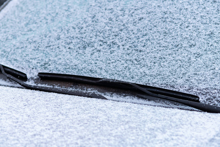 雪覆盖的车窗与雨刷宏观关闭。 防冻液没有使用。 雪地里的车辆。 冬天的时间来了。 恶劣天气条件