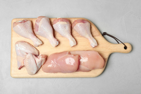 木制木板，带有生鸡胸，翅膀和鸡腿，灰色背景，俯视