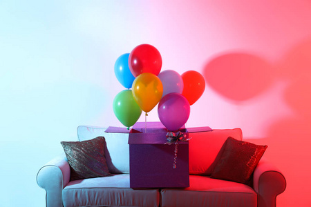 带有彩色背景沙发上明亮气球的礼品盒