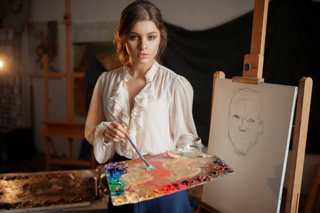 女画家与调色板和刷子站在画架在工作室。 创意绘画女人画铅笔素描车间内部背景