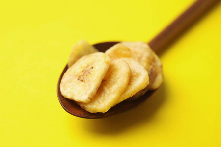 彩色背景上带有香蕉片的木勺，特写..干果作为健康小吃