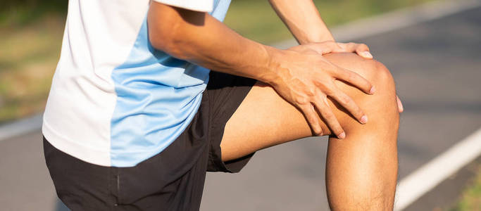年轻的健身男子抱着他的运动腿受伤。 训练过程中肌肉疼痛。 亚洲跑步者在外面早上跑步和锻炼后膝盖疼痛和问题。 运动和健康概念