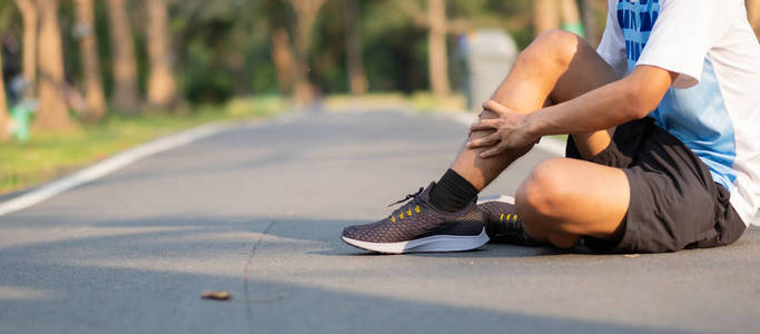 年轻的健身男子抱着他的运动腿受伤。 训练过程中肌肉疼痛。 亚洲跑步者在外面早上跑步和锻炼后小腿疼痛和问题。 运动和健康概念