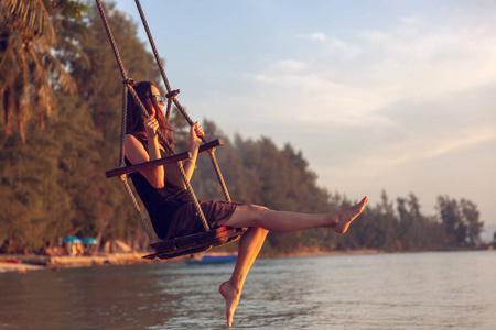 年轻美丽的快乐女人在日落时在海滩上荡秋千，放松旅行生活方式的概念