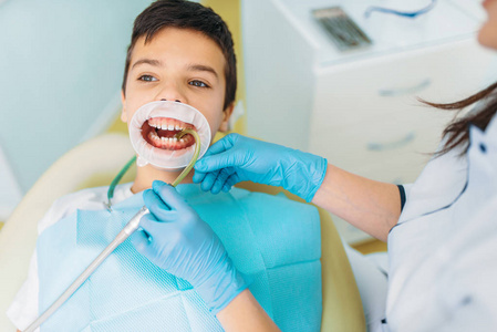 小男孩在一个牙科橱柜龋齿去除程序儿童牙科。 女牙医与儿童合作
