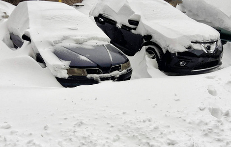 在十二月降雪期间，住宅区的停车场上覆盖着雪的汽车。