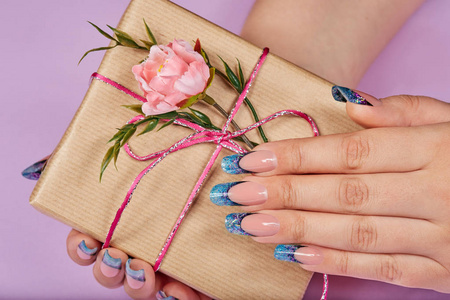 双手用蓝色人造法式指甲，手里拿着礼品盒，有蝴蝶结和粉红色的花