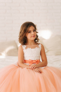 棕色头发的小漂亮女孩穿着桃色的连衣裙。坐在沙发上的女孩