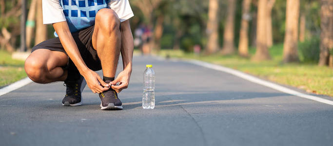 年轻的运动员在公园户外系跑鞋。 男跑运动员准备在外面的路上慢跑。 亚洲健身步行和晨间步道锻炼。 健康和体育概念